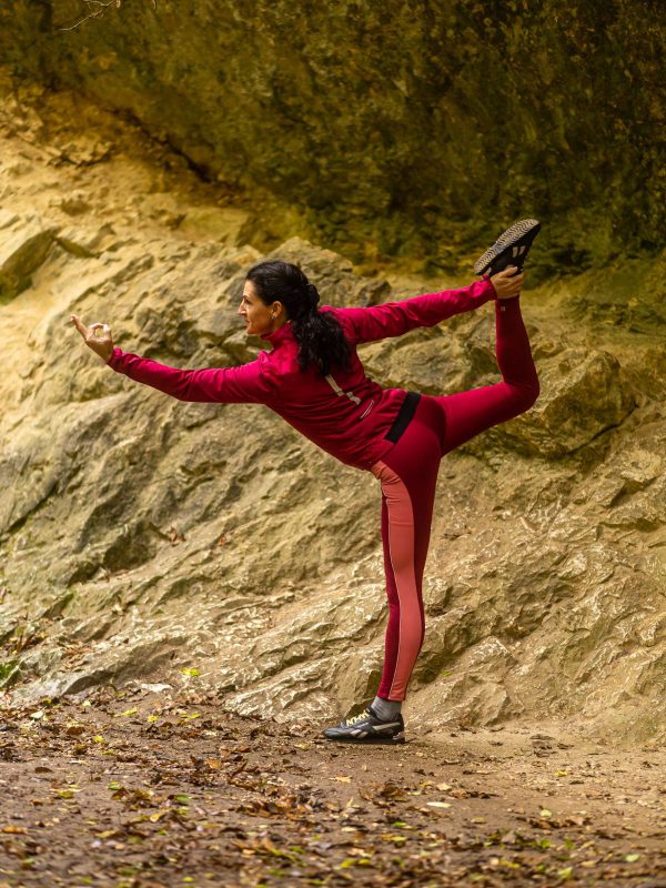 Jógázó nő táncos pózban (natarajasana) sziklás túraútvonalon